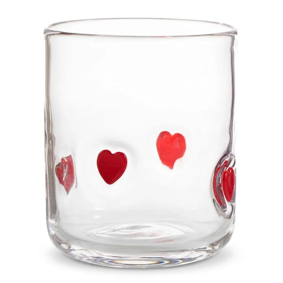 A clear glass tumbler with three red heart designs on the front, photographed against a solid white background.