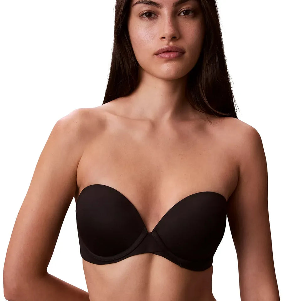 A woman modeling a black strapless bandeau-style bra against a plain white background.