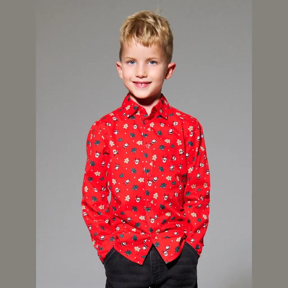 A young boy with blonde hair wearing a red long-sleeve button-down shirt with a small multicolor floral pattern, paired with black pants, standing against a solid gray studio background.