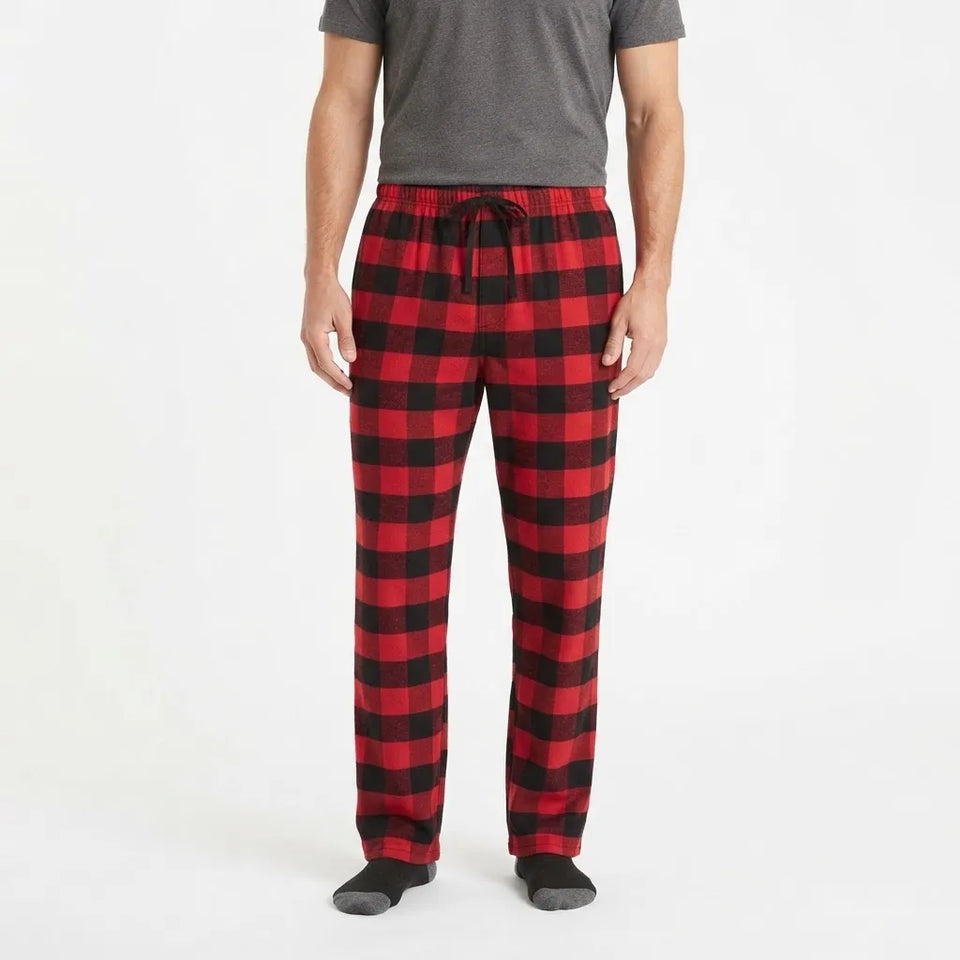 A man wearing red and black buffalo plaid pajama pants with a drawstring waist, paired with a gray t-shirt and dark socks, shown from the waist down on a white studio background.