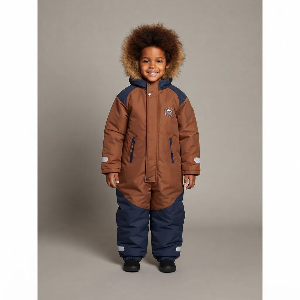 A young child wearing a brown and navy winter snowsuit with a fluffy brown faux-fur trimmed hood, standing against a neutral gray studio background.