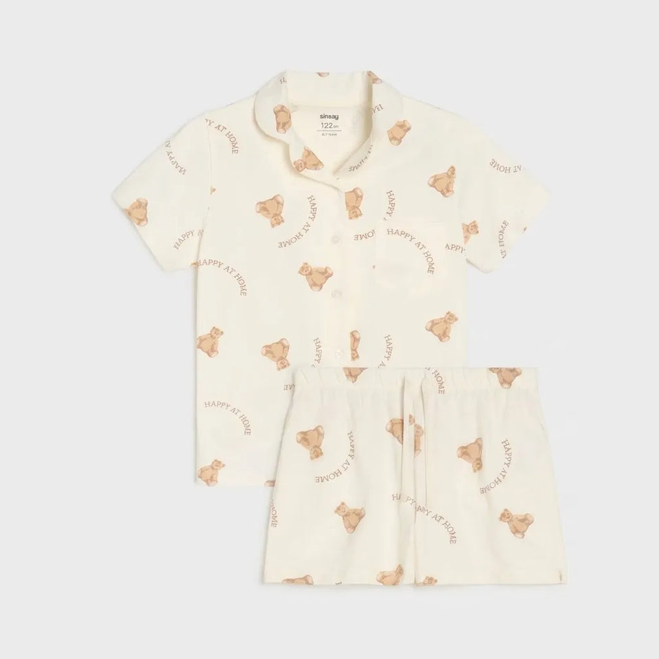 A two-piece baby pajama set featuring a short-sleeve button-front top and matching shorts in cream, decorated with a repeating pattern of teddy bears and the text 'HAPPY BAT TIME'.