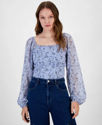Woman wearing a blue floral blouse and dark jeans on a white background