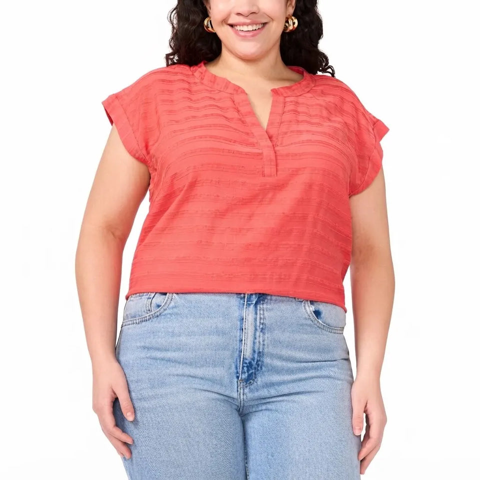 A woman wearing a coral pink short-sleeve textured top with a split neckline and light blue jeans, shown from the waist up against a plain white background.