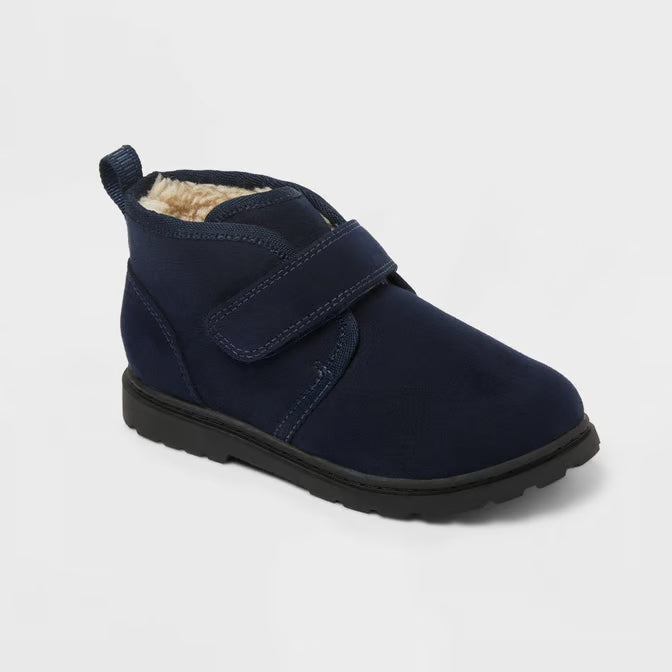 A navy blue ankle boot for toddlers, featuring a velcro strap, a soft beige faux-fur lining, and a black sole, shown on a light gray background.