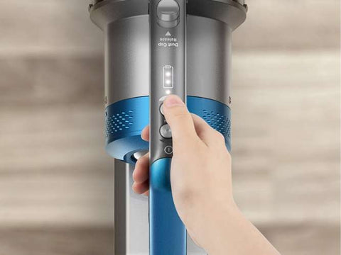 Hand operating a blue and silver vacuum cleaner on a neutral background