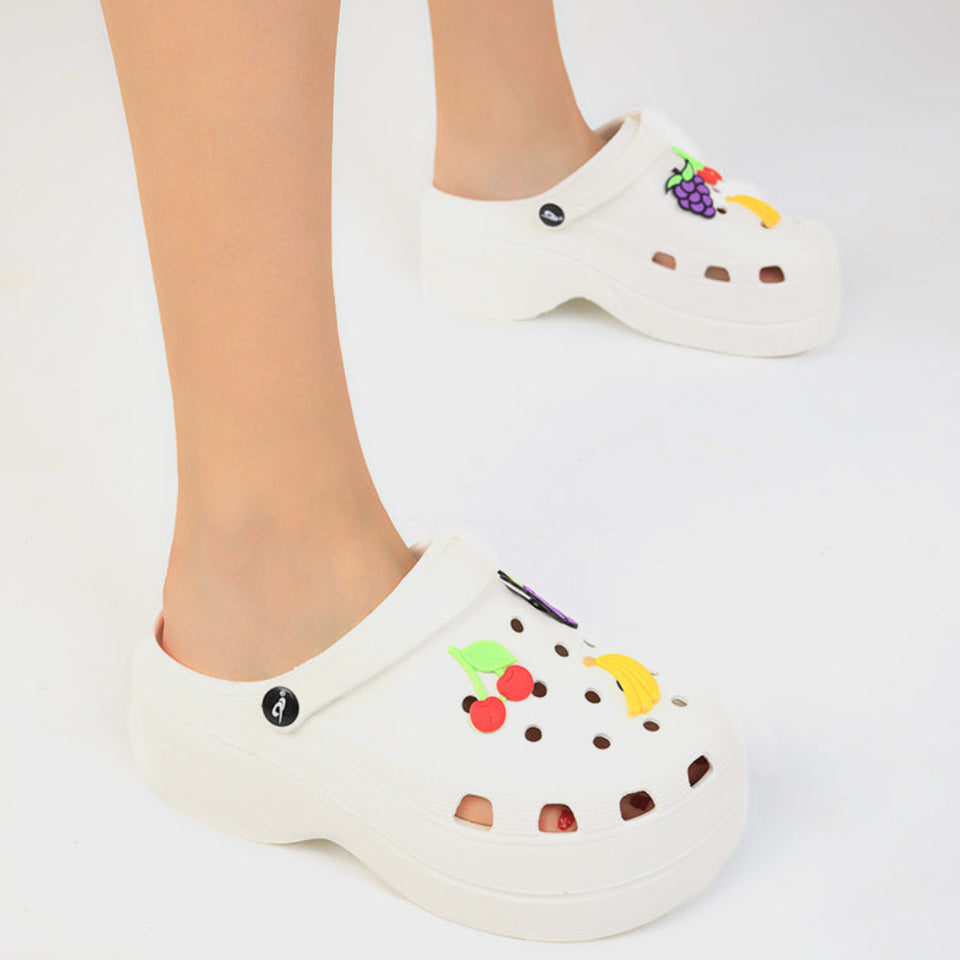 White foam clogs with colorful fruit charms, shown on a person's feet against a plain white background.