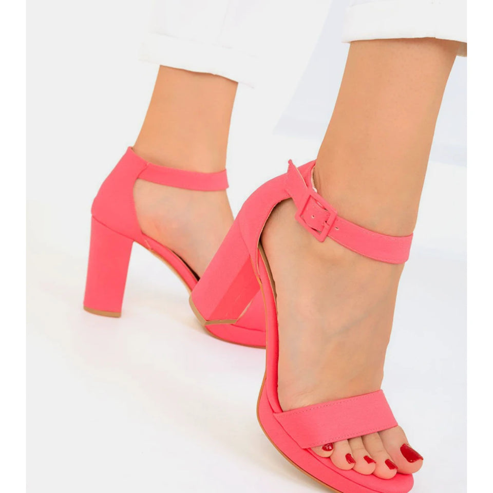 A pair of women's bright pink block-heel sandals with ankle straps and open toes, shown on a model's feet against a clean white background.