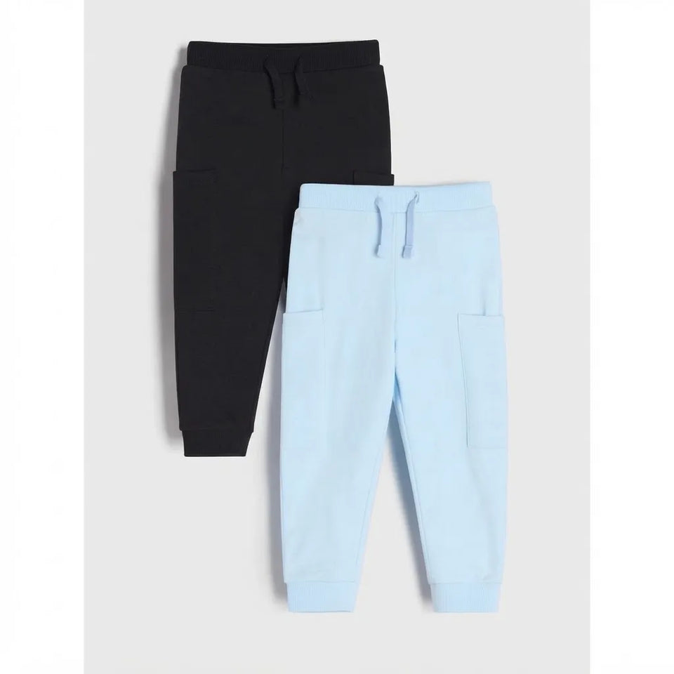 Two pairs of children's jogger sweatpants laid flat on a light gray background: one in black and one in light blue. Both have elastic waistbands with drawstrings and side patch pockets.