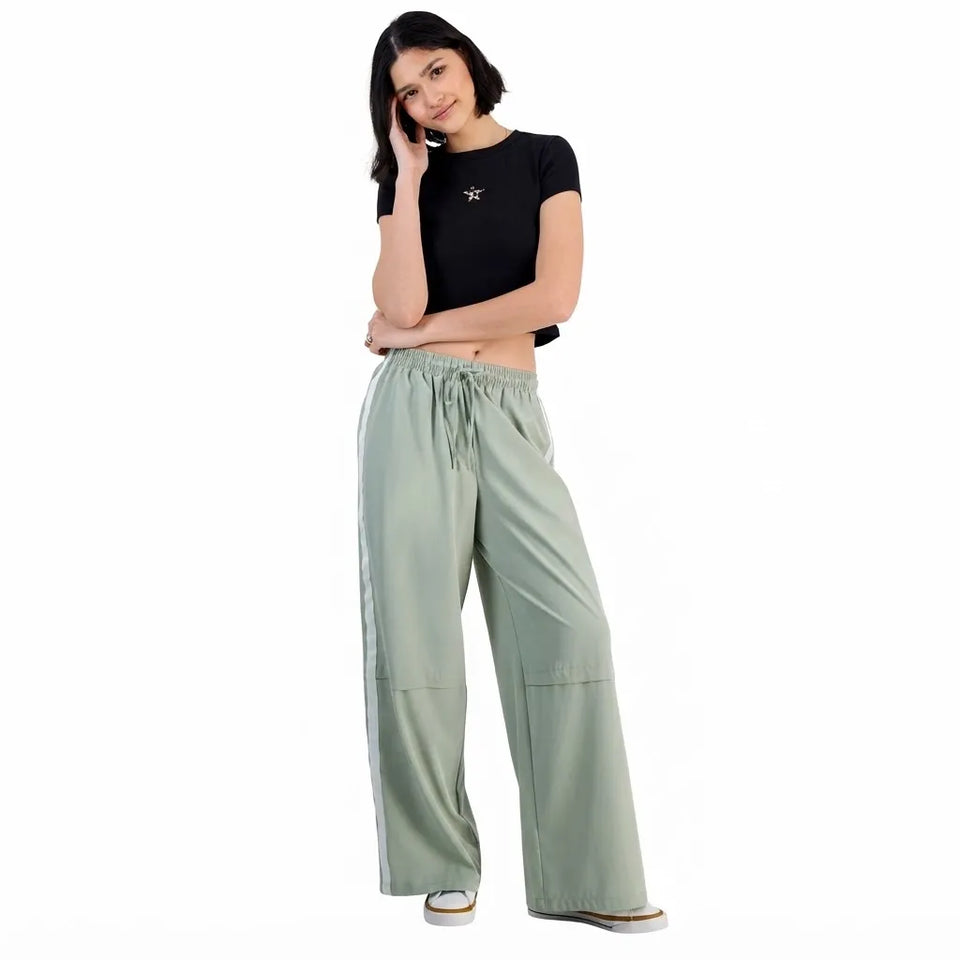 A woman modeling a black short-sleeve crop top and sage green wide-leg drawstring pants against a plain white background.