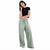 A woman modeling a black short-sleeve crop top and sage green wide-leg drawstring pants against a plain white background.