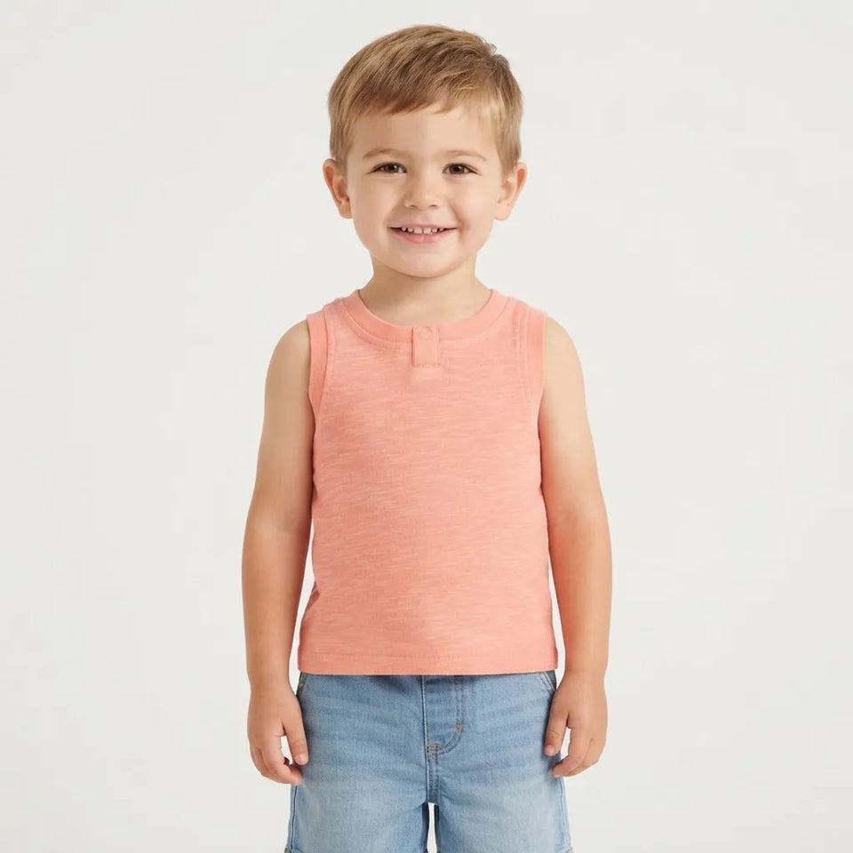 A young boy wearing a sleeveless peach-colored henley tank top and light blue jeans, standing against a plain white studio background.