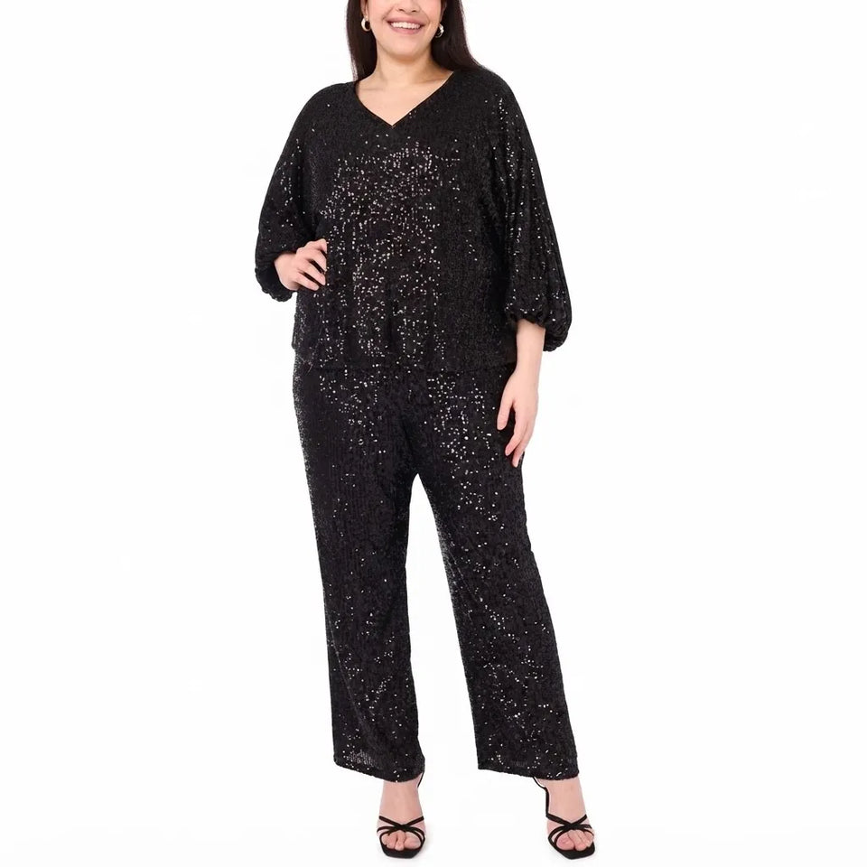 A woman modeling a black sequined jumpsuit with a V-neck and elbow-length sleeves, paired with black strappy heels, against a plain white background.