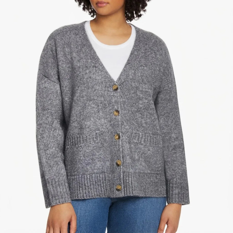 A woman wearing a gray heathered knit cardigan with brown buttons over a white crewneck shirt and blue jeans, shown from the mouth down on a plain white background.