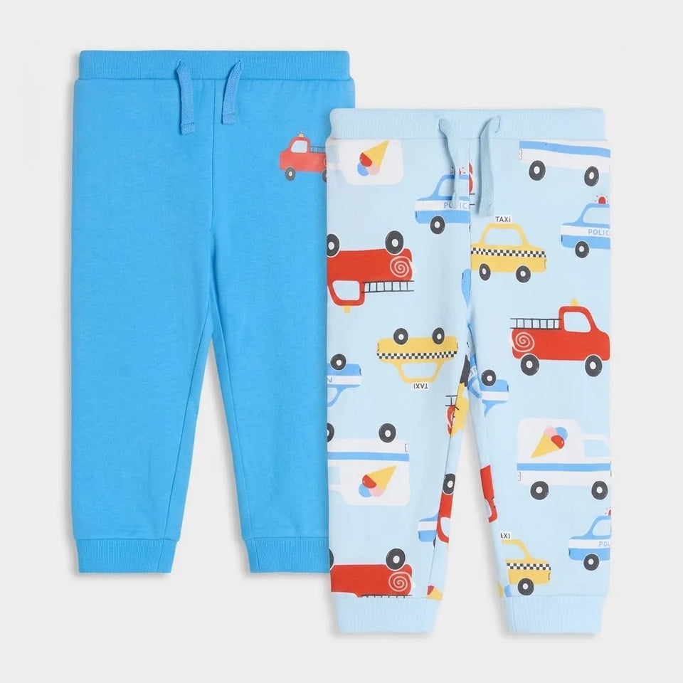 Two pairs of children's sweatpants laid flat on a light gray background. One pair is solid bright blue with a drawstring waist, and the other pair is light blue with a colorful pattern of cartoon vehicles including taxis, fire trucks, and police cars.