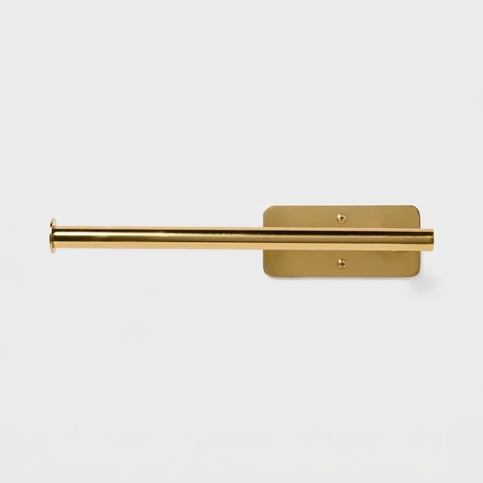 A polished brass wall-mounted toilet paper holder with a horizontal rod and a rectangular backplate, shown against a light gray background.