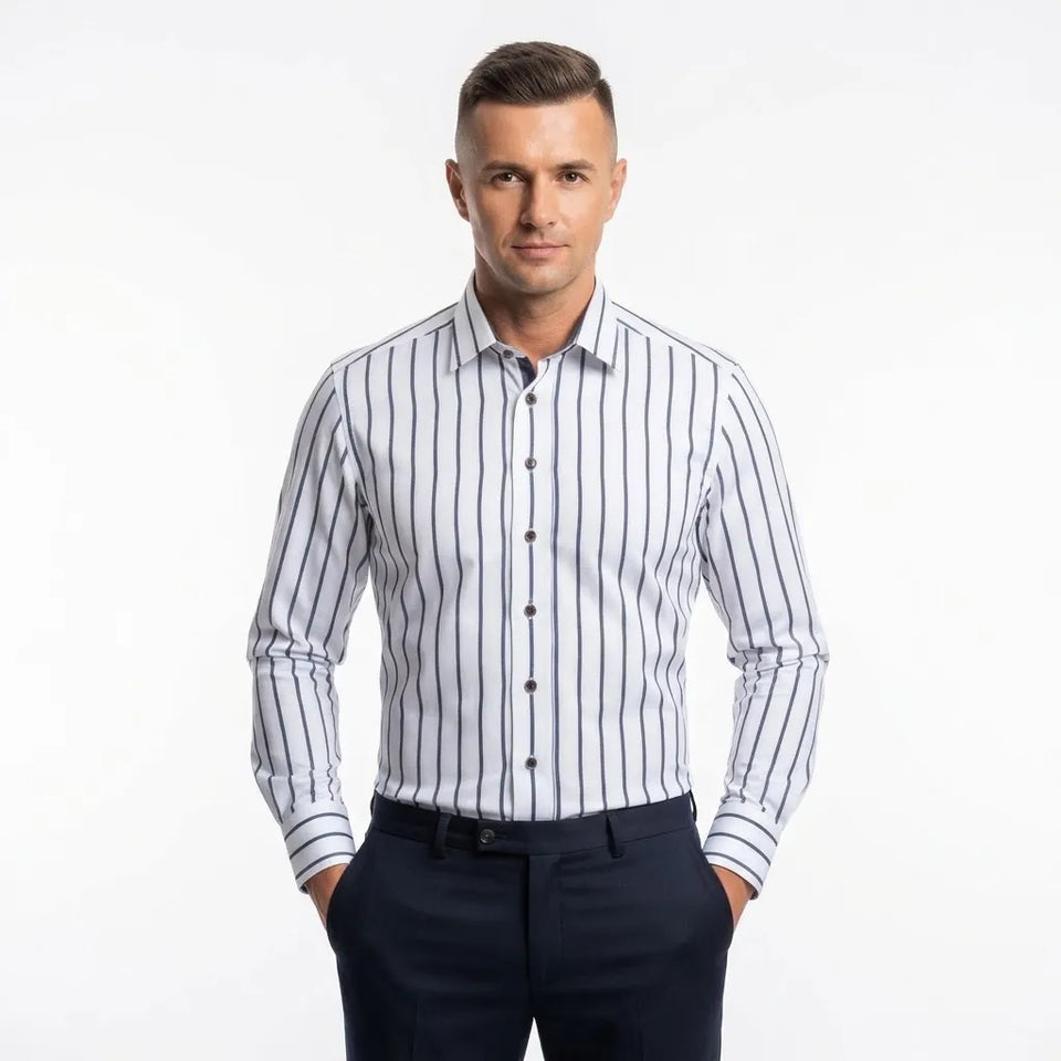A man wearing a long-sleeve button-down dress shirt with thin vertical navy blue stripes on a white background, paired with dark navy trousers, against a plain white studio background.