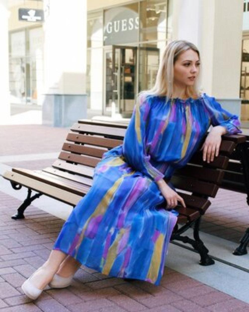 Woman in a colorful dress sitting on a bench in front of a Guess store.