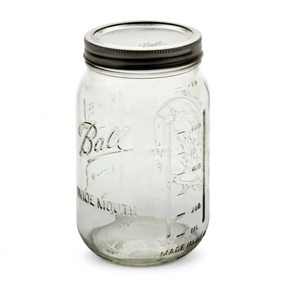 A clear glass Ball mason jar with embossed lettering and measurement markings, featuring a dark metal screw-on lid, shown on a plain white background.