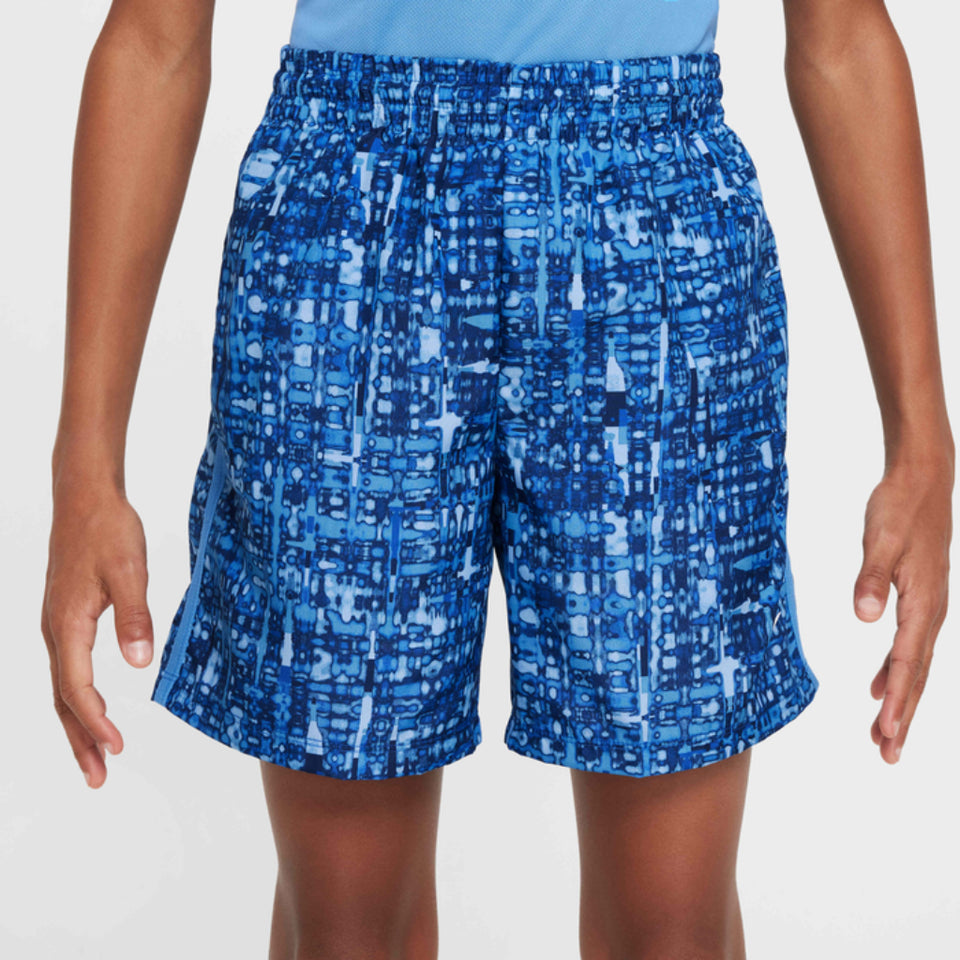 A person wearing blue athletic shorts with an abstract geometric print in shades of blue and white, shown from the waist to mid-thigh against a light gray studio background.