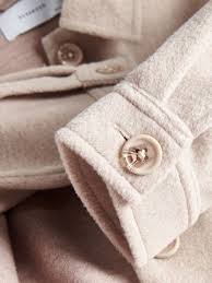 Close-up of a beige coat with buttons and a label on a neutral background