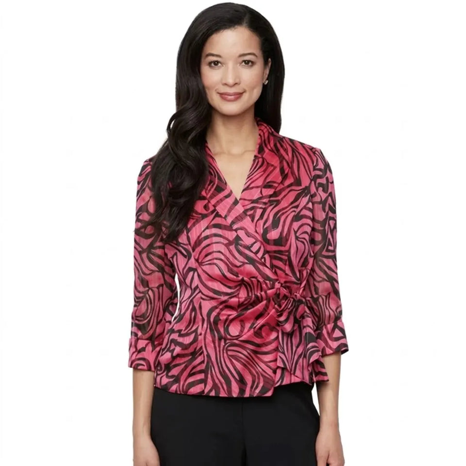A woman modeling a pink and black abstract patterned wrap-style blouse with three-quarter sleeves, paired with black pants, against a plain white background.