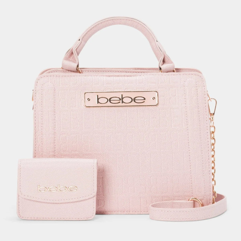 A light pink textured handbag with a matching small wallet and a long shoulder strap, displayed on a clean light gray background. The handbag features a top handle, a gold-tone chain detail, and a metal plate with the brand name 'bebe'.