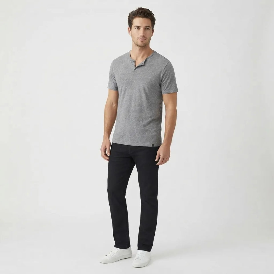 A man modeling a short-sleeve gray henley t-shirt, black pants, and white sneakers against a plain white studio background.