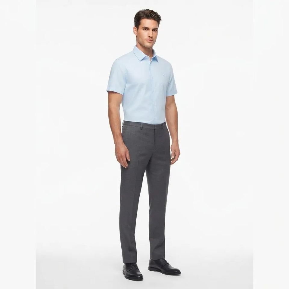 A man modeling a light blue short-sleeve button-down shirt and dark gray dress pants against a plain white studio background.