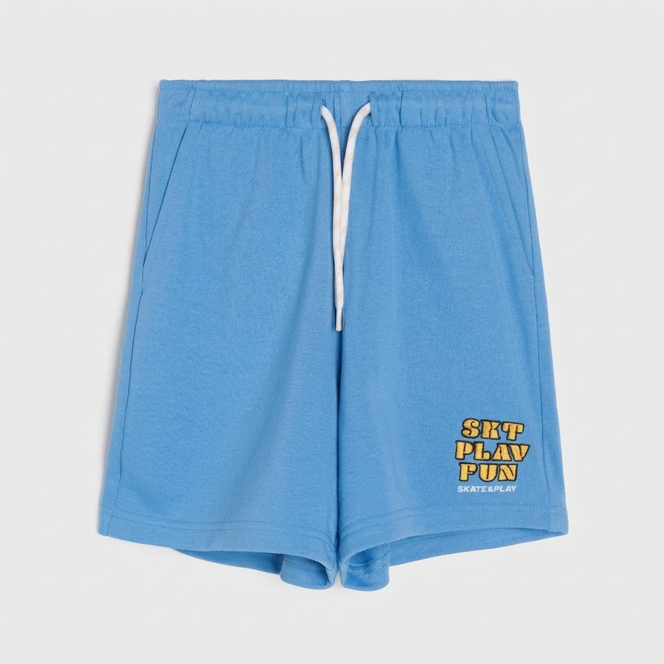Light blue sweat shorts with a white drawstring and a yellow and black 'SKATE PLAY FUN' graphic on the lower left leg, shown against a light gray background.