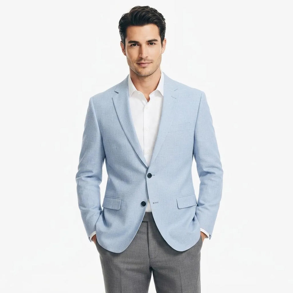A man wearing a light blue blazer over a white dress shirt and gray trousers, standing against a plain white studio background.