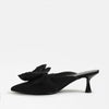 A single black pointed-toe mule heel with a large fabric bow detail on the vamp, shown in profile against a clean white background.