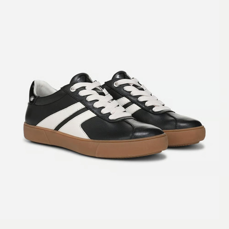 A pair of low-top leather sneakers in black and white with a brown gum sole, shown from a three-quarters angle on a light gray background.