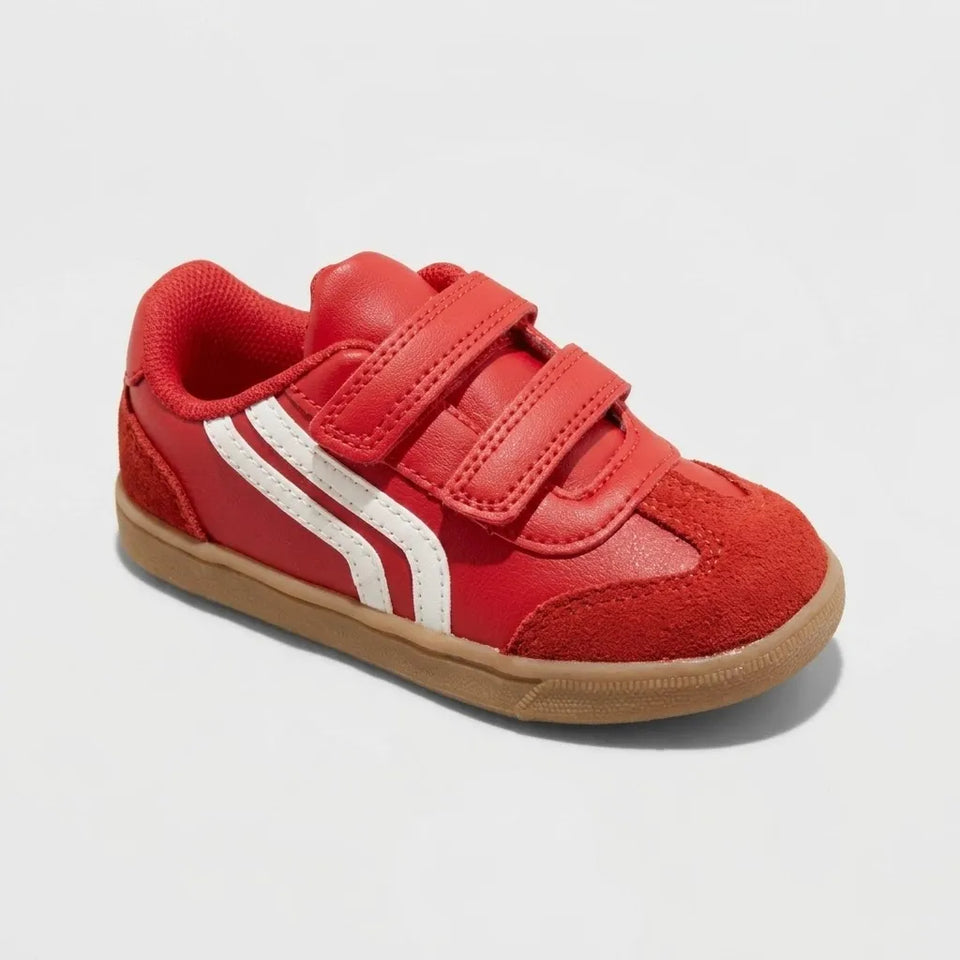 A red toddler sneaker with two hook-and-loop straps, a white side stripe, and a tan rubber sole, shown on a light gray background.
