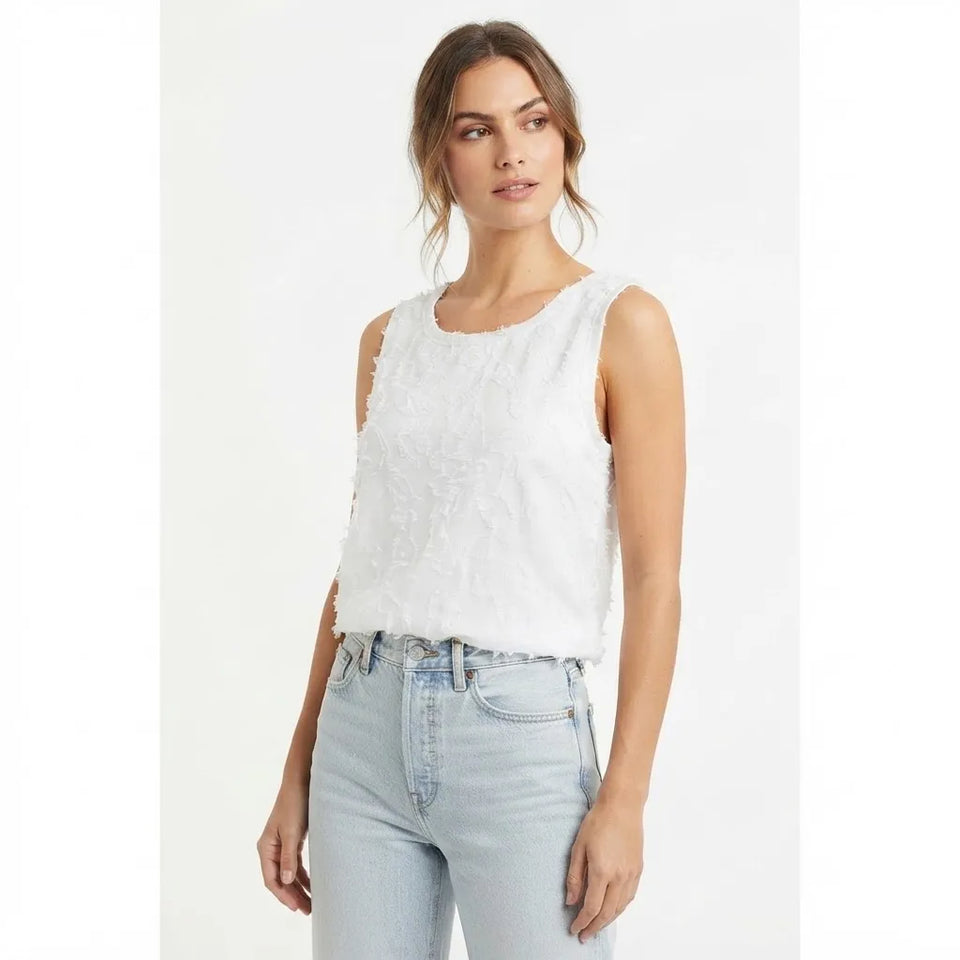 A woman modeling a sleeveless white textured top with light-wash blue jeans against a plain white studio background.