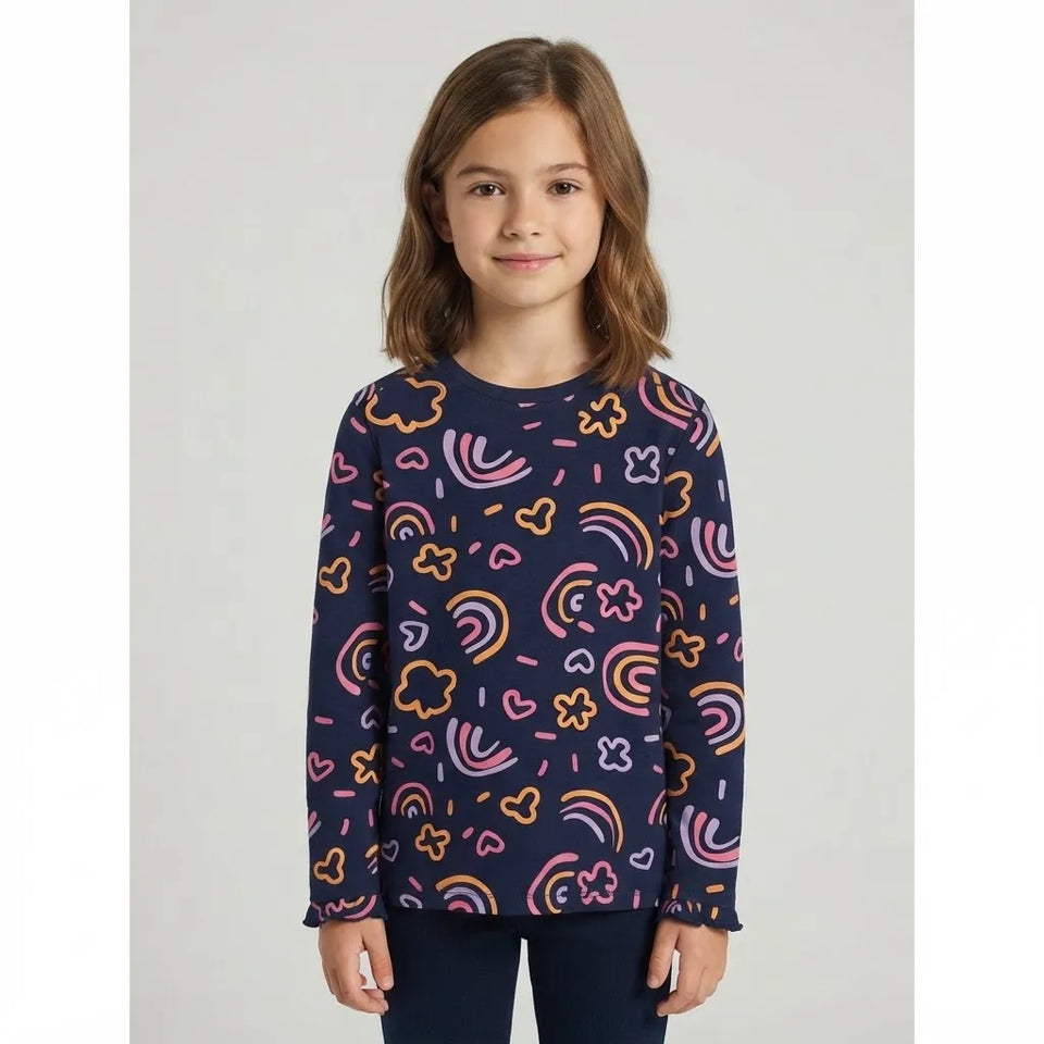 A young girl with light brown hair wearing a navy blue long-sleeve top with a colorful rainbow and heart pattern, paired with dark blue pants, standing against a light gray background.