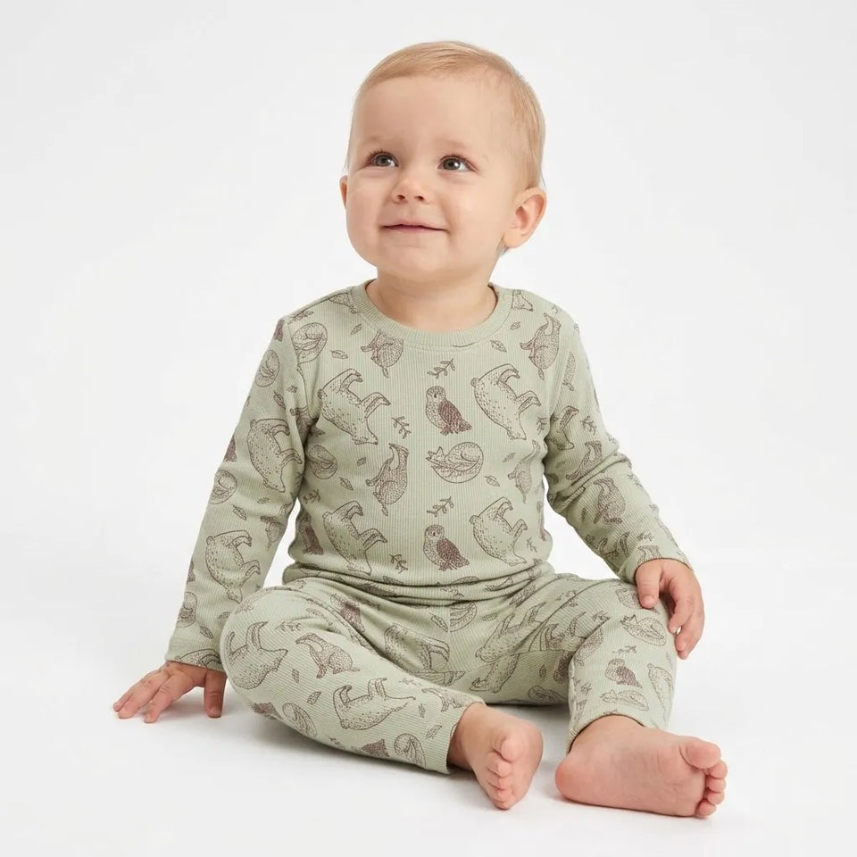 A baby sitting on a white studio background wearing a sage green long-sleeve pajama set with a brown animal print.