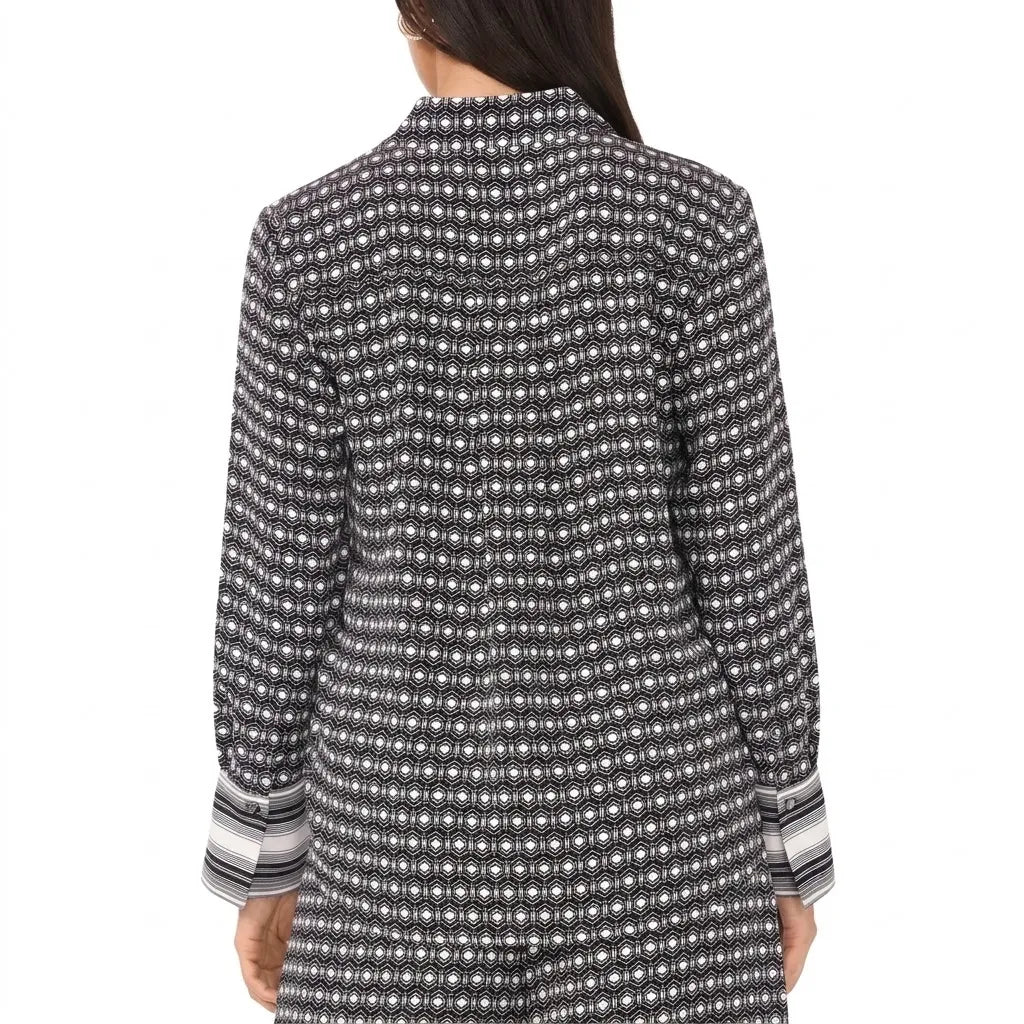 A woman shown from the back wearing a long-sleeve button-front tunic or shirt with an allover small white geometric dot pattern on a black or charcoal base, plus striped cuffs.