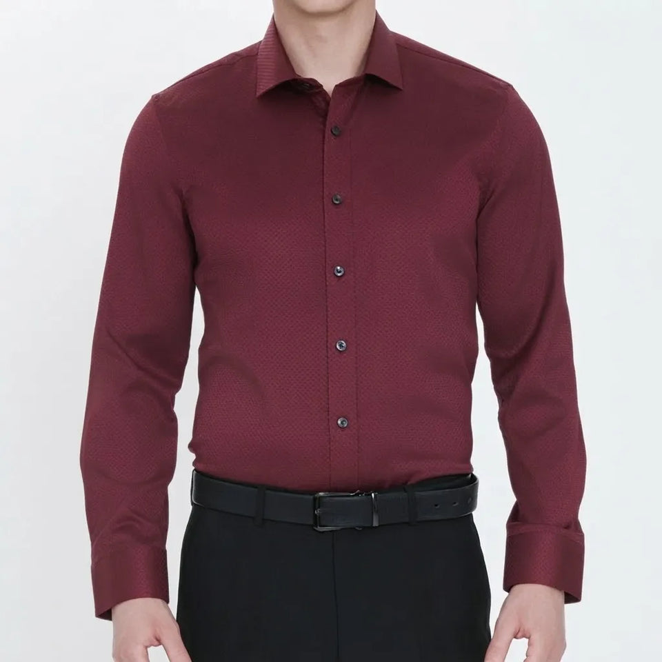 A man wearing a long-sleeve button-down dress shirt in burgundy with a subtle textured pattern, paired with black trousers and a black belt, shown from the neck down against a plain white background.