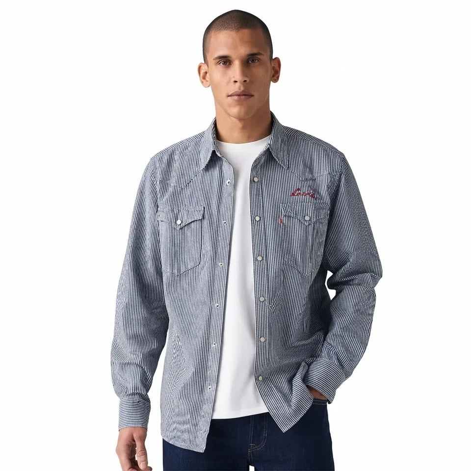 A man wearing a blue and white vertically striped western-style button-up shirt over a white t-shirt and dark jeans, photographed against a plain white background.