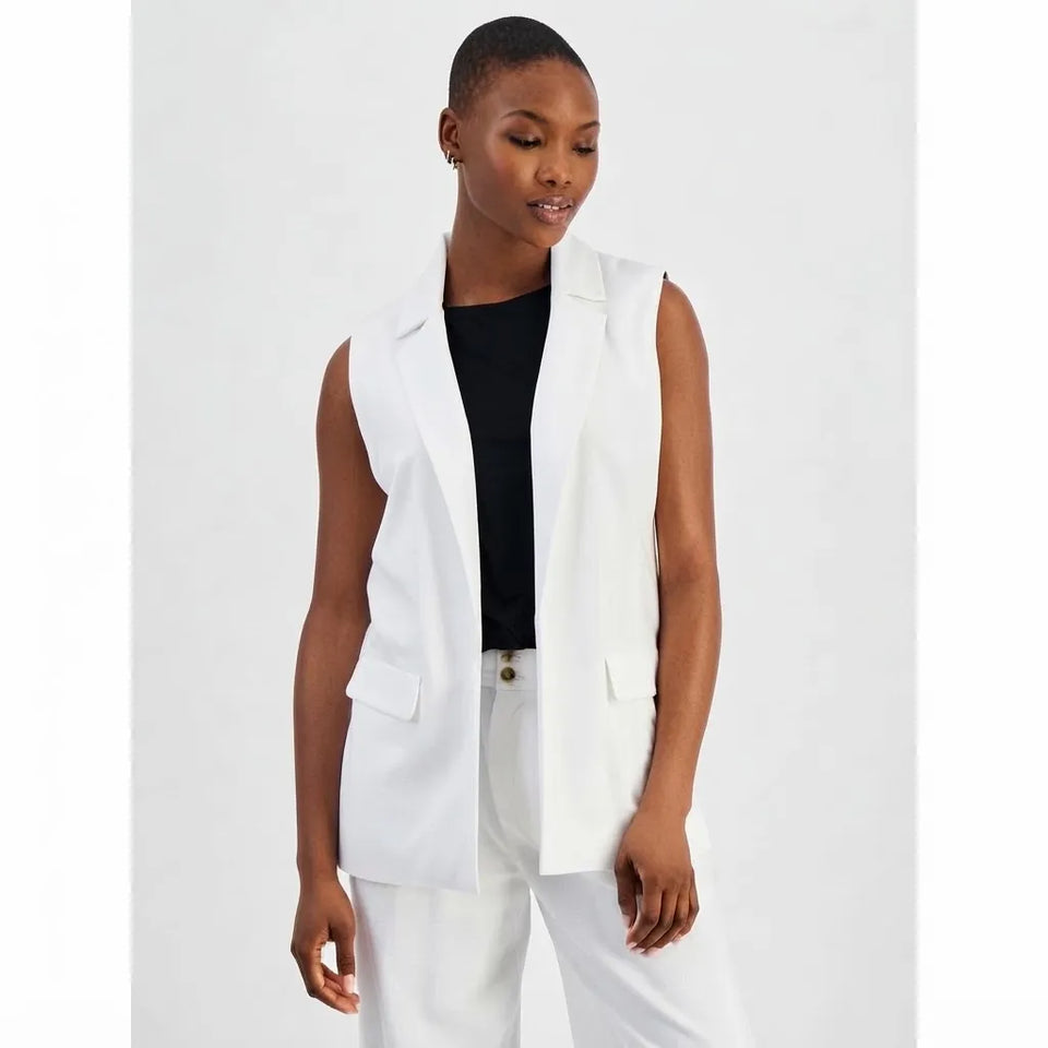 A woman modeling a white sleeveless blazer vest over a black top and white trousers, photographed against a plain light gray studio background.