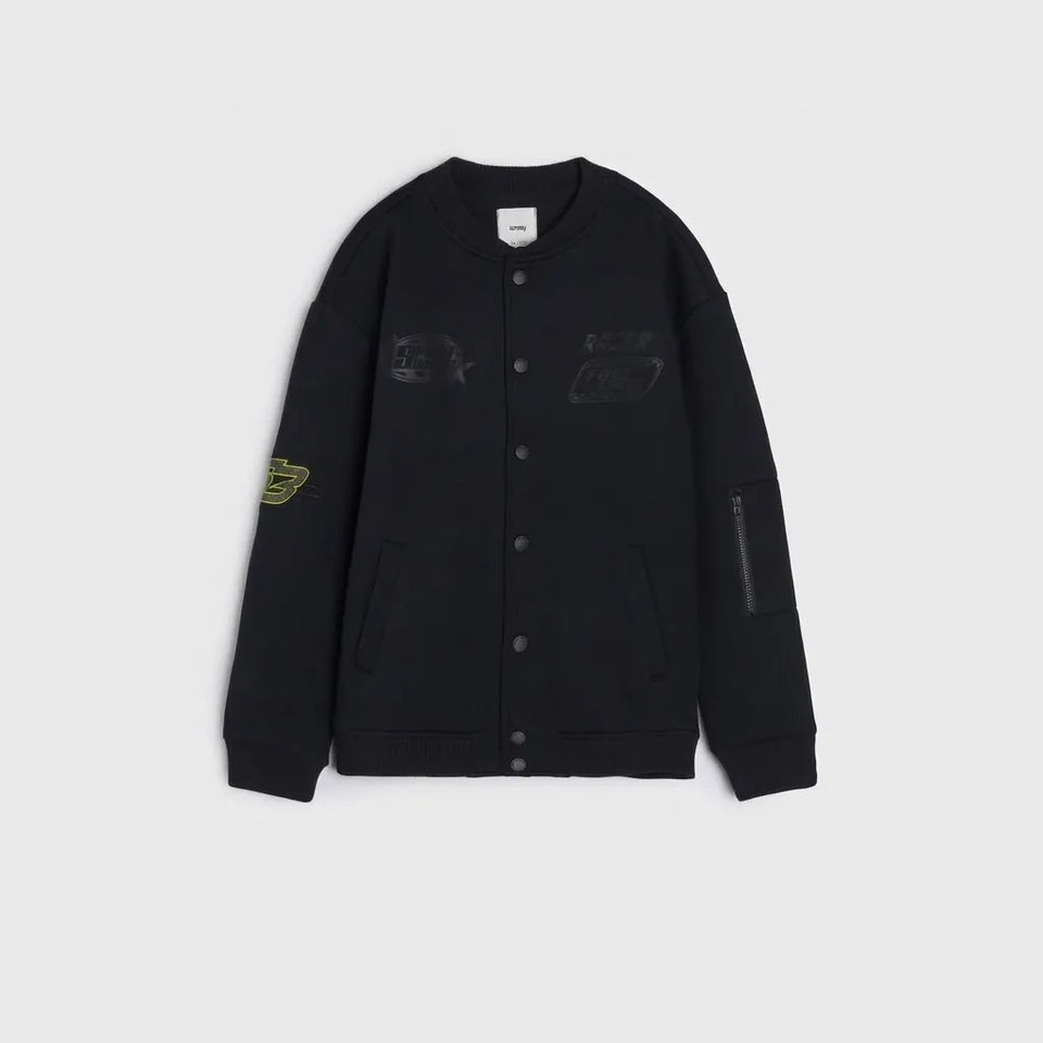 A black varsity-style jacket with button-front closure, ribbed cuffs and hem, and multiple graphic patches on the chest and sleeves, shown flat against a light gray background.