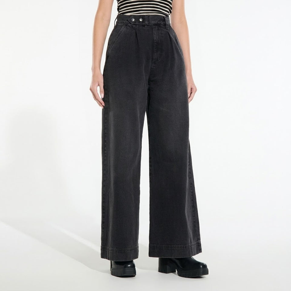 A model wearing high-waisted, wide-leg charcoal gray denim pants with a striped top and black platform shoes, photographed against a clean white studio background.