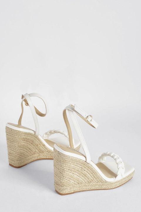 White wedge sandals with espadrille sole on a light gray background