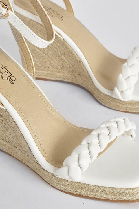 White wedge sandals with braided design on a light gray background