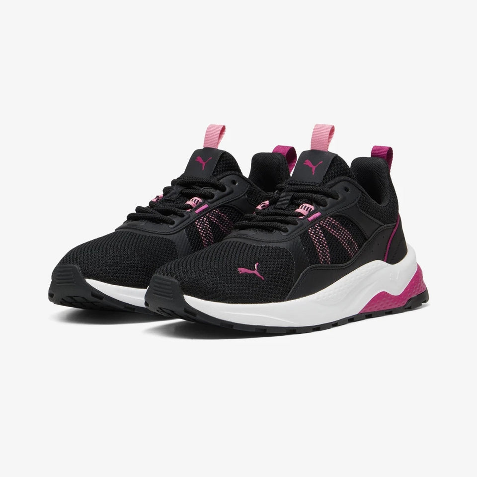 A pair of Puma sneakers in black and white with vibrant pink accents, including the Puma logo, heel detail, and pull tabs, shown on a light gray background.