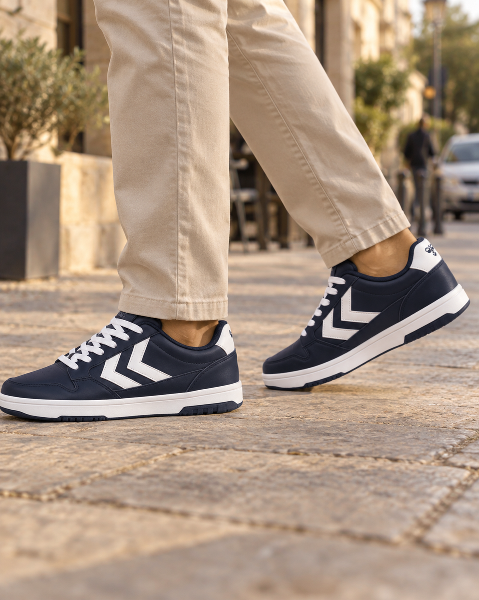 Hummel navy Nielsen sneakers worn with beige trousers on a stone sidewalk