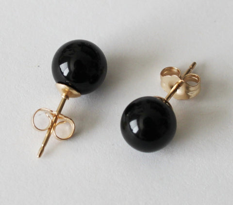Black round earrings with gold posts on a light gray background