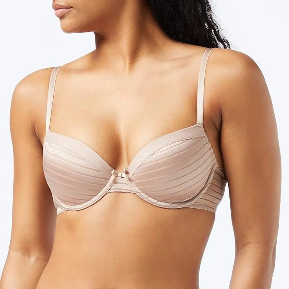 A close-up of a woman wearing a light beige/nude wireless bra with thin straps and a small center charm, shown against a plain light background.
