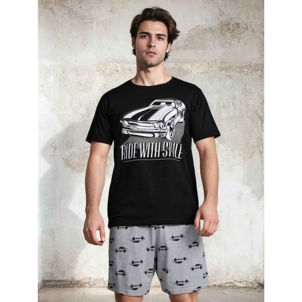 A man modeling a black short-sleeve graphic t-shirt with a white car print and the text 'RIDE WITH STYLE', paired with gray shorts featuring a black car pattern, set against a textured concrete wall.